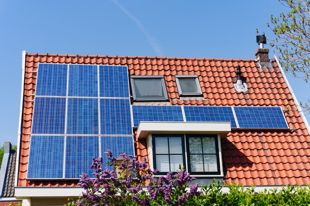 Solar panel on a red roof reflecting the sun and the cloudless blue sky